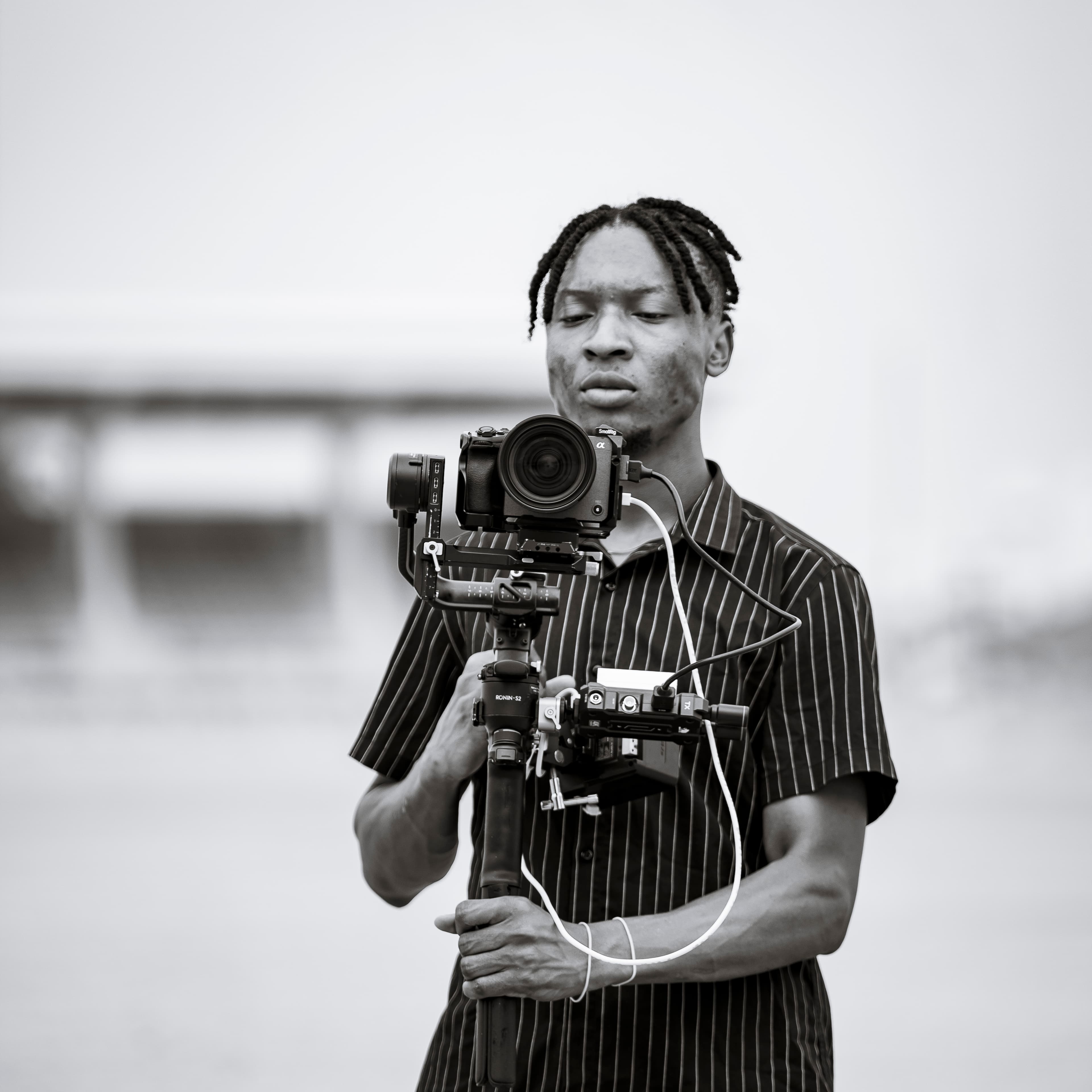 Black-and-white frame of the filmmaker holding the gimbal rig at chest height, looking past the lens