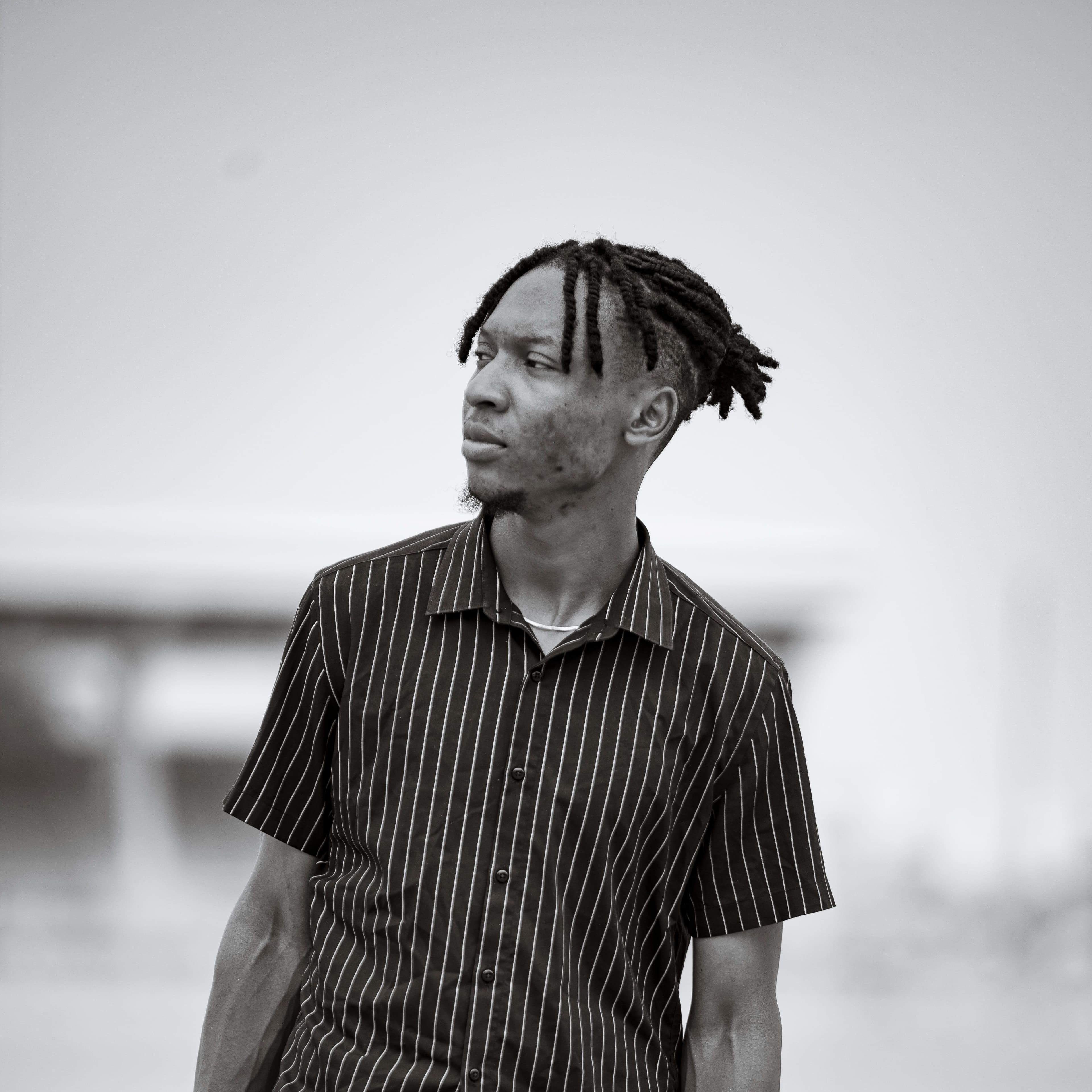 Black-and-white portrait of a filmmaker in a pinstriped shirt, looking off to his left against a blown-out sky