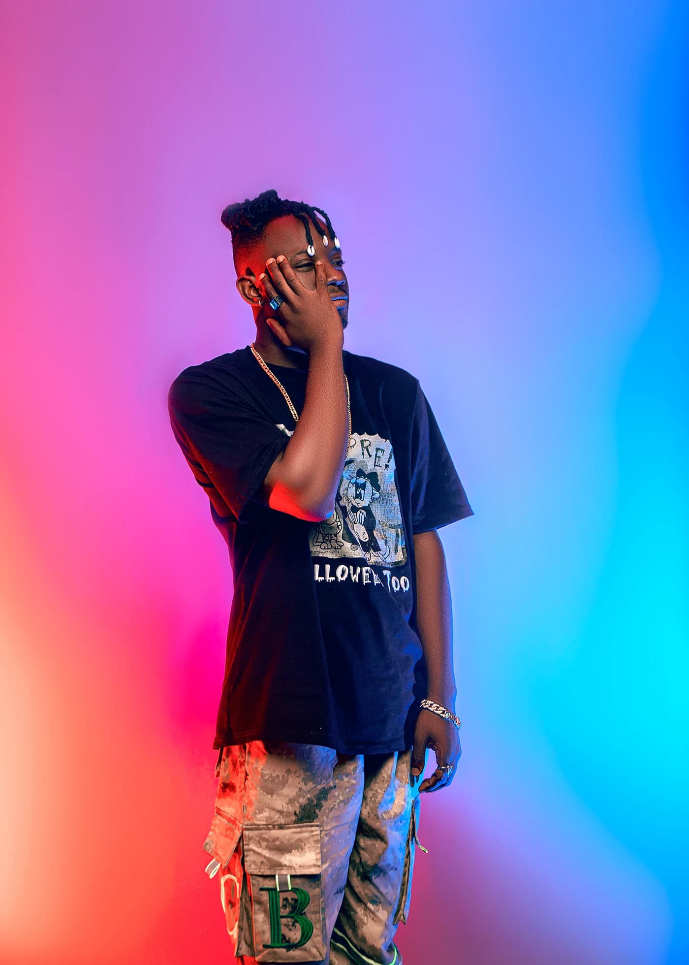 Full-length against a backdrop washed red to blue, one hand raised to his face