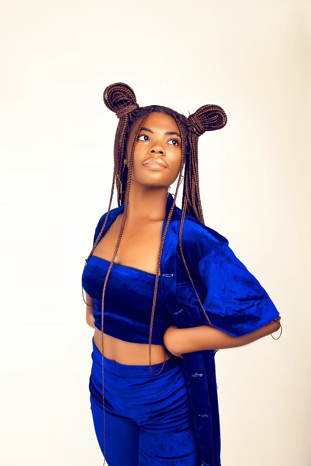 Standing in a blue velvet co-ord and open jacket, chin lifted, looking off past the light
