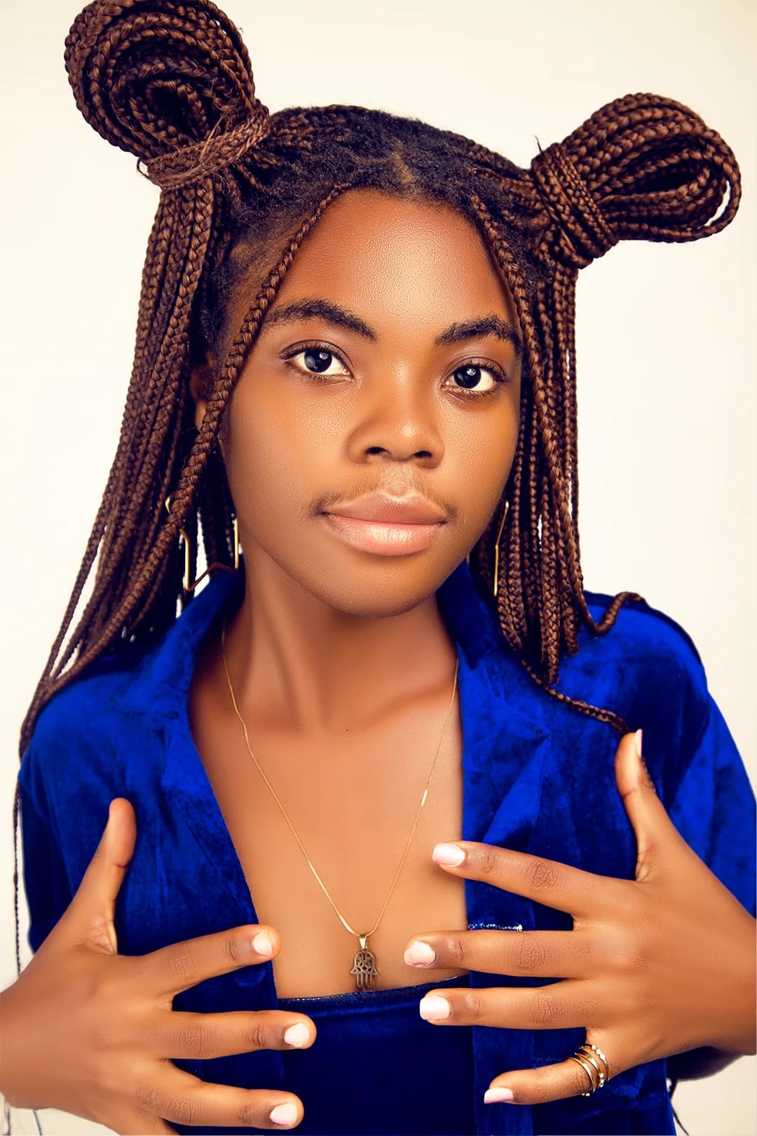 Tight beauty portrait, braided hair in twin buns, blue velvet jacket held open, looking straight to camera