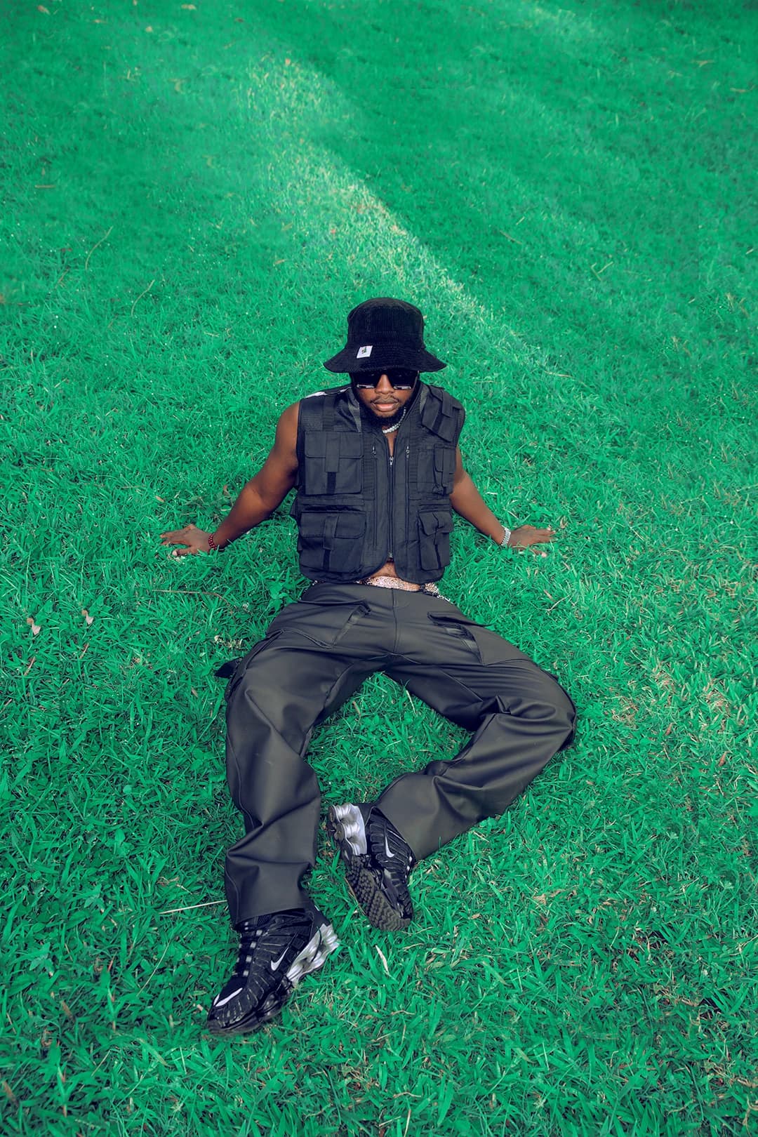 Overhead shot of the artist lying back on bright green grass, arms open