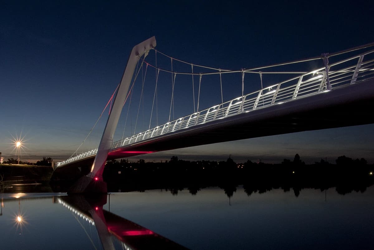 The footbridge from the bank, its single mast raking across a deep blue sky